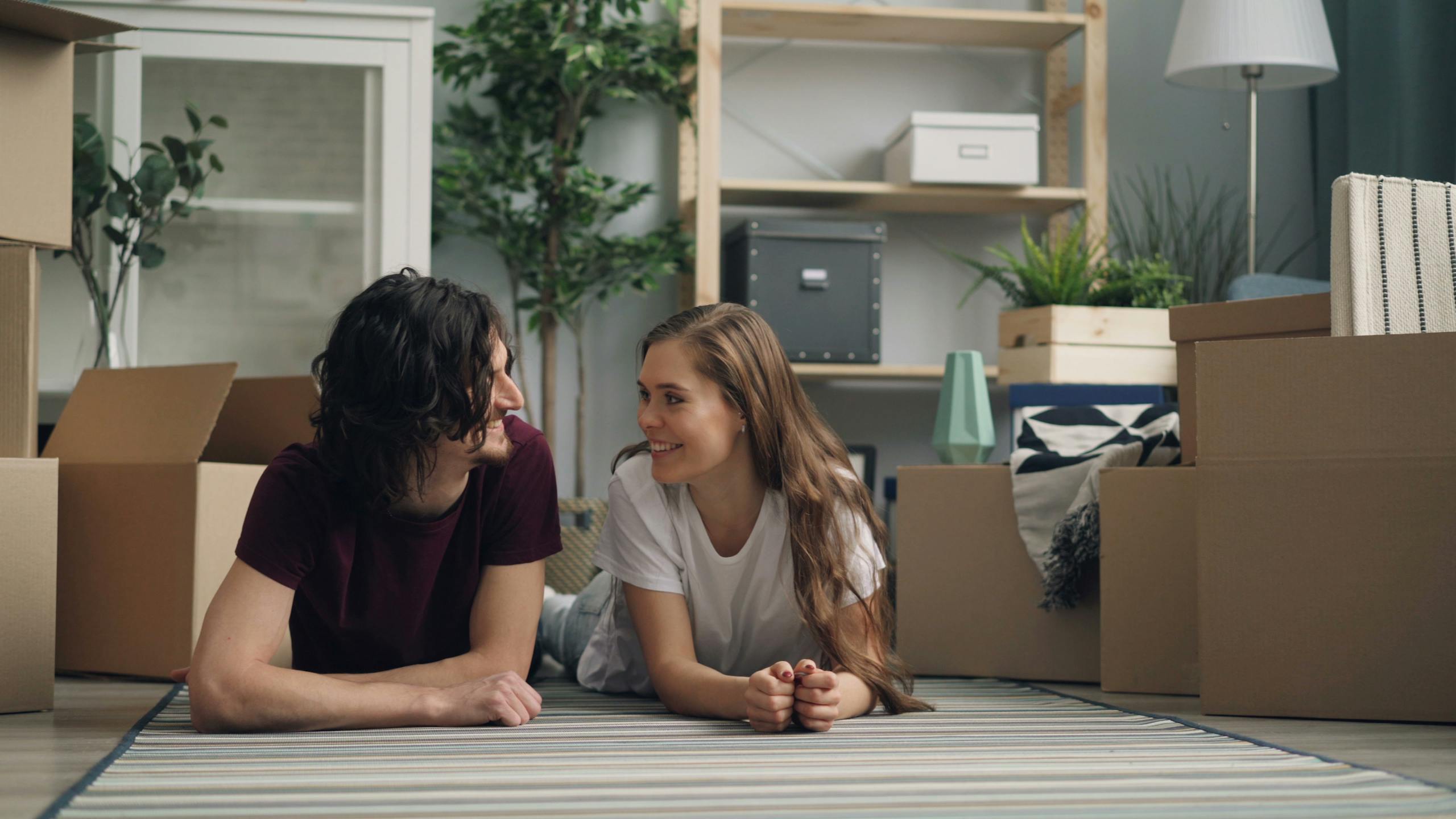 Happy couple lying on the floor surrounded by moving boxes in their new home.