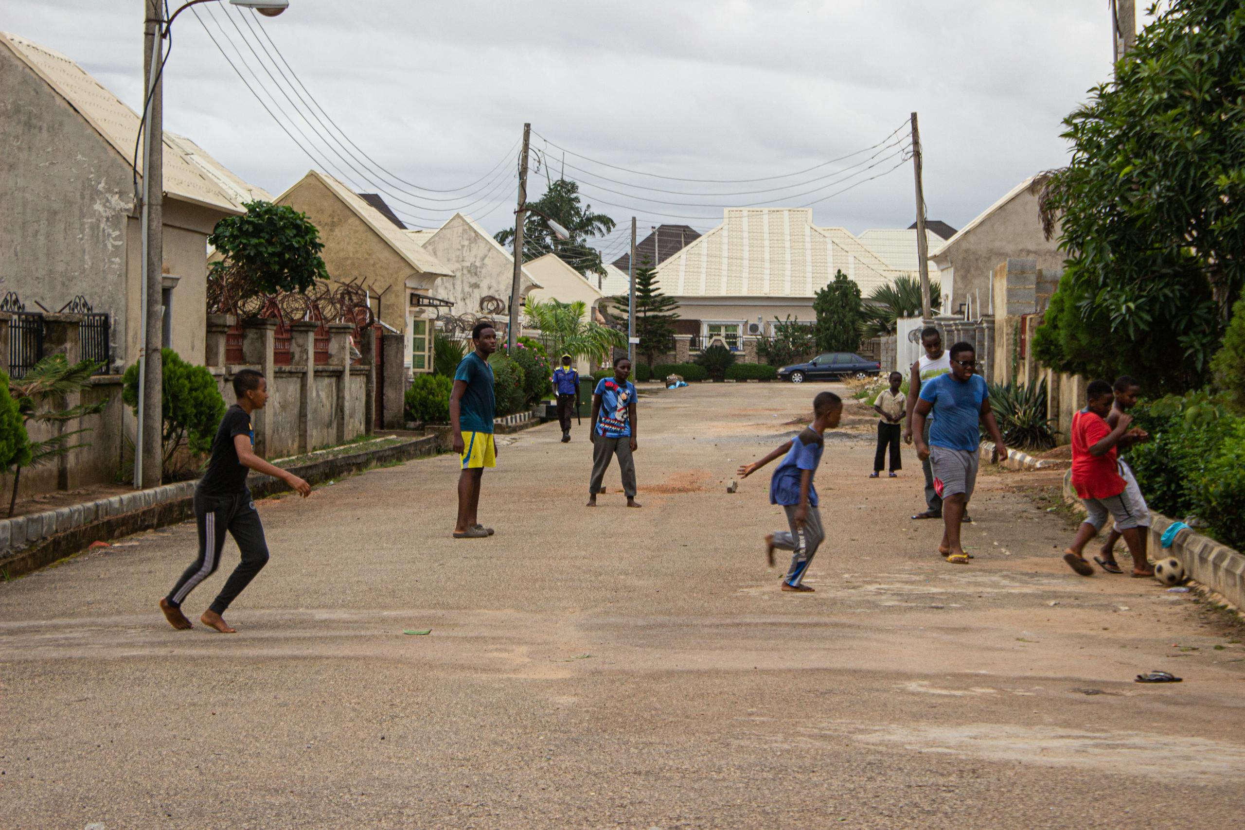 Kids playing football on a quiet street in Abuja, Nigeria, capturing lively outdoor activities.