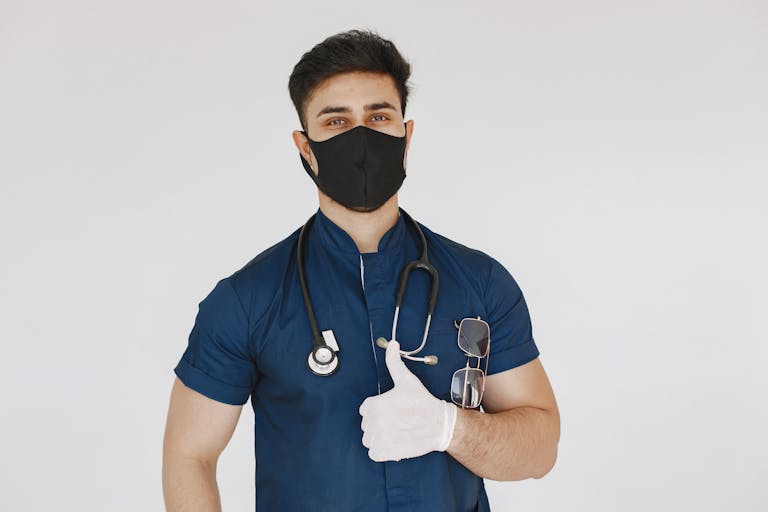Male nurse wearing mask and gloves giving a thumbs up gesture confidently.