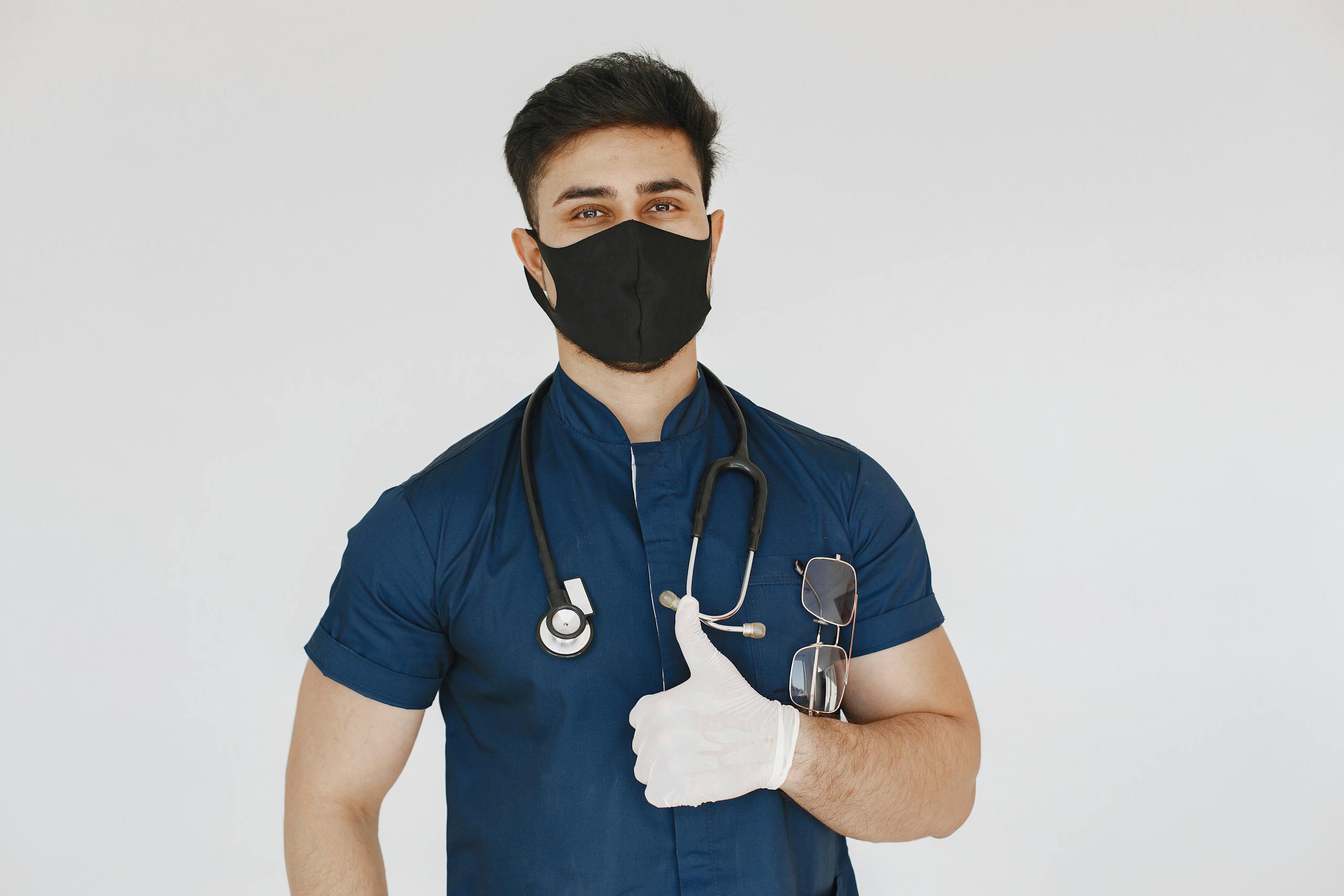 Male nurse wearing mask and gloves giving a thumbs up gesture confidently.