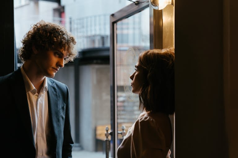 Man and woman dressed elegantly in conversation by a doorway, creating a romantic atmosphere.