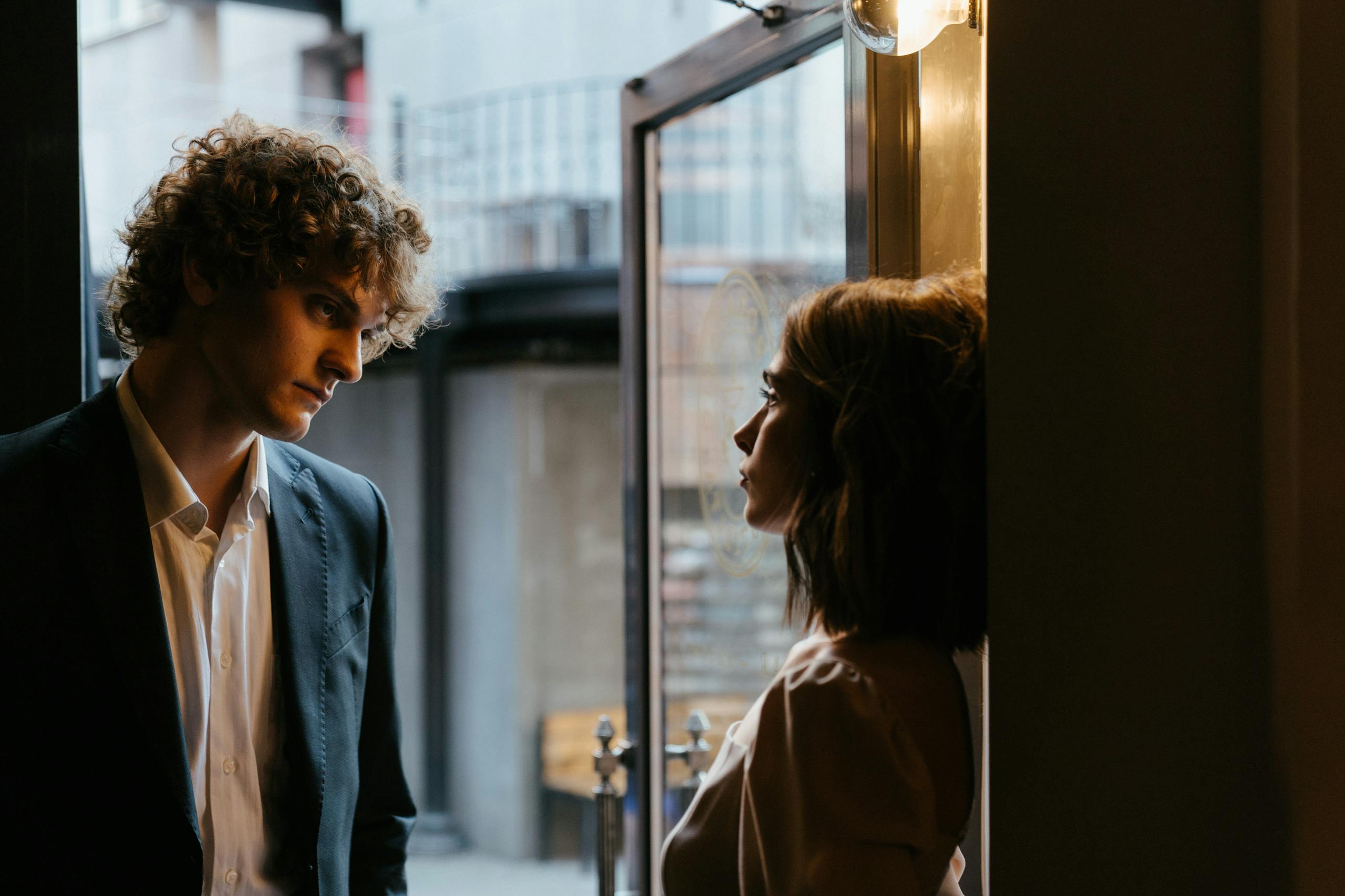 Man and woman dressed elegantly in conversation by a doorway, creating a romantic atmosphere.