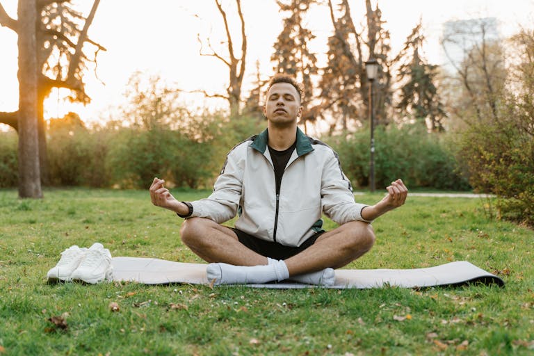 Man meditating outdoors in a tranquil park setting at sunset, promoting relaxation and mindfulness.