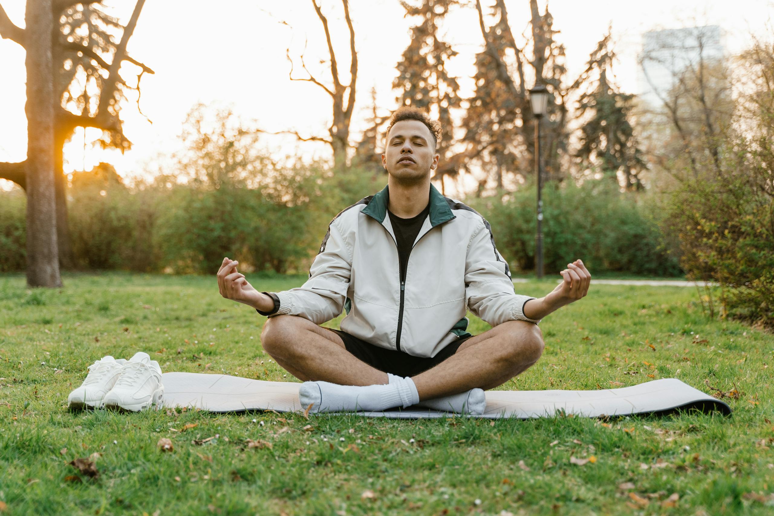 Man meditating outdoors in a tranquil park setting at sunset, promoting relaxation and mindfulness.