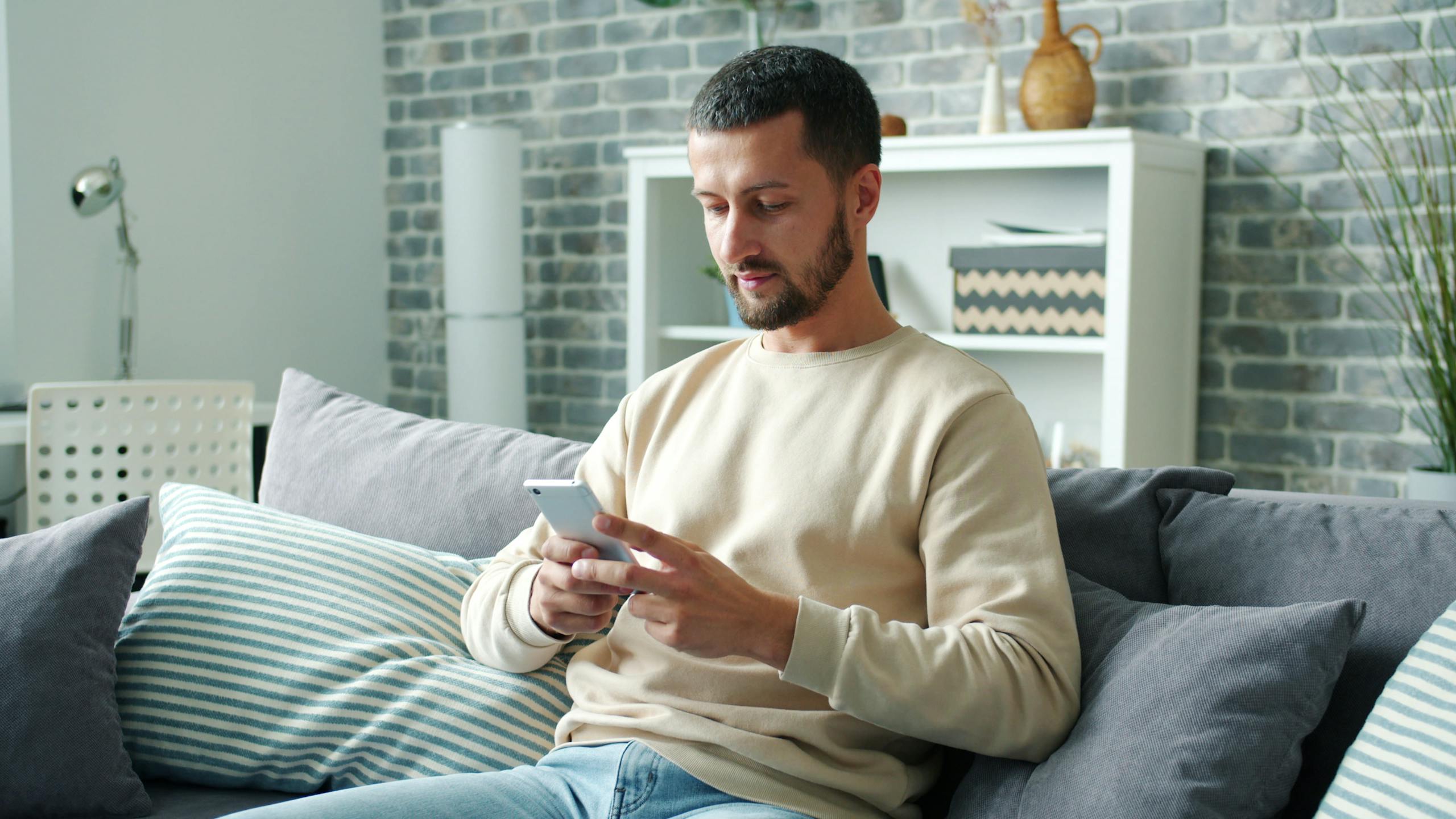 Man sitting on a couch using a smartphone in a cozy living room setting.