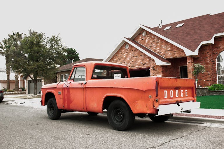 Old red Dodge truck parked in a quiet suburban neighborhood street.