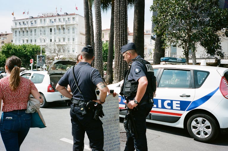 Police officers and a civilian interact near a police car on a busy city street.