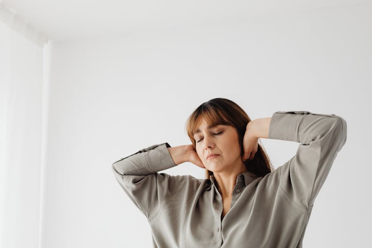 Portrait of a relaxed woman with eyes closed and hands behind head, in a serene indoor setting with white background.