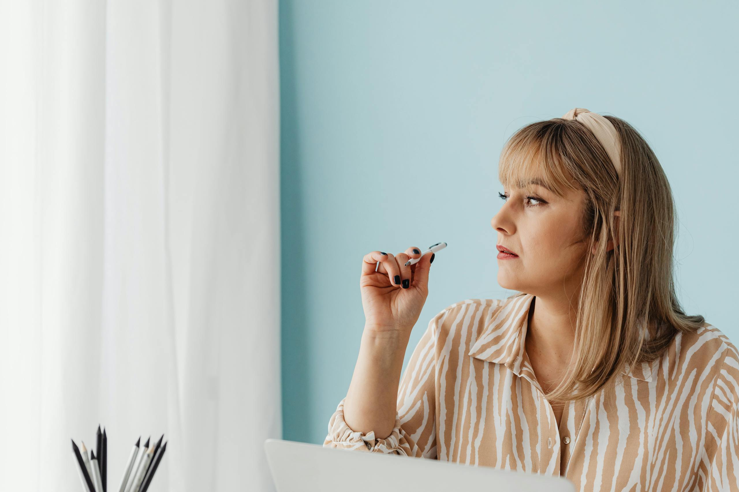 Portrait of a woman with blonde hair thoughtfully holding a pen in an office setting. Perfect for workplace themes.