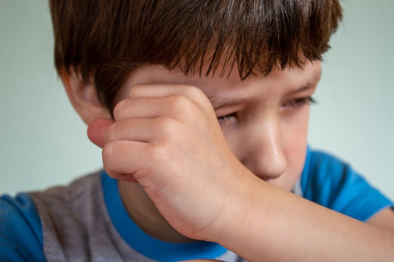 Portrait of crop upset little child with brown hair crying and wiping tears from face against white background