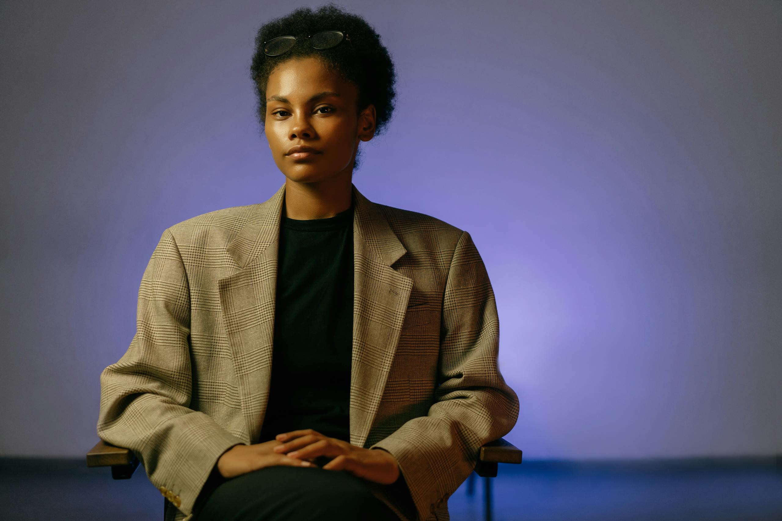 Professional woman with curly hair and eyeglasses sitting confidently in a studio.