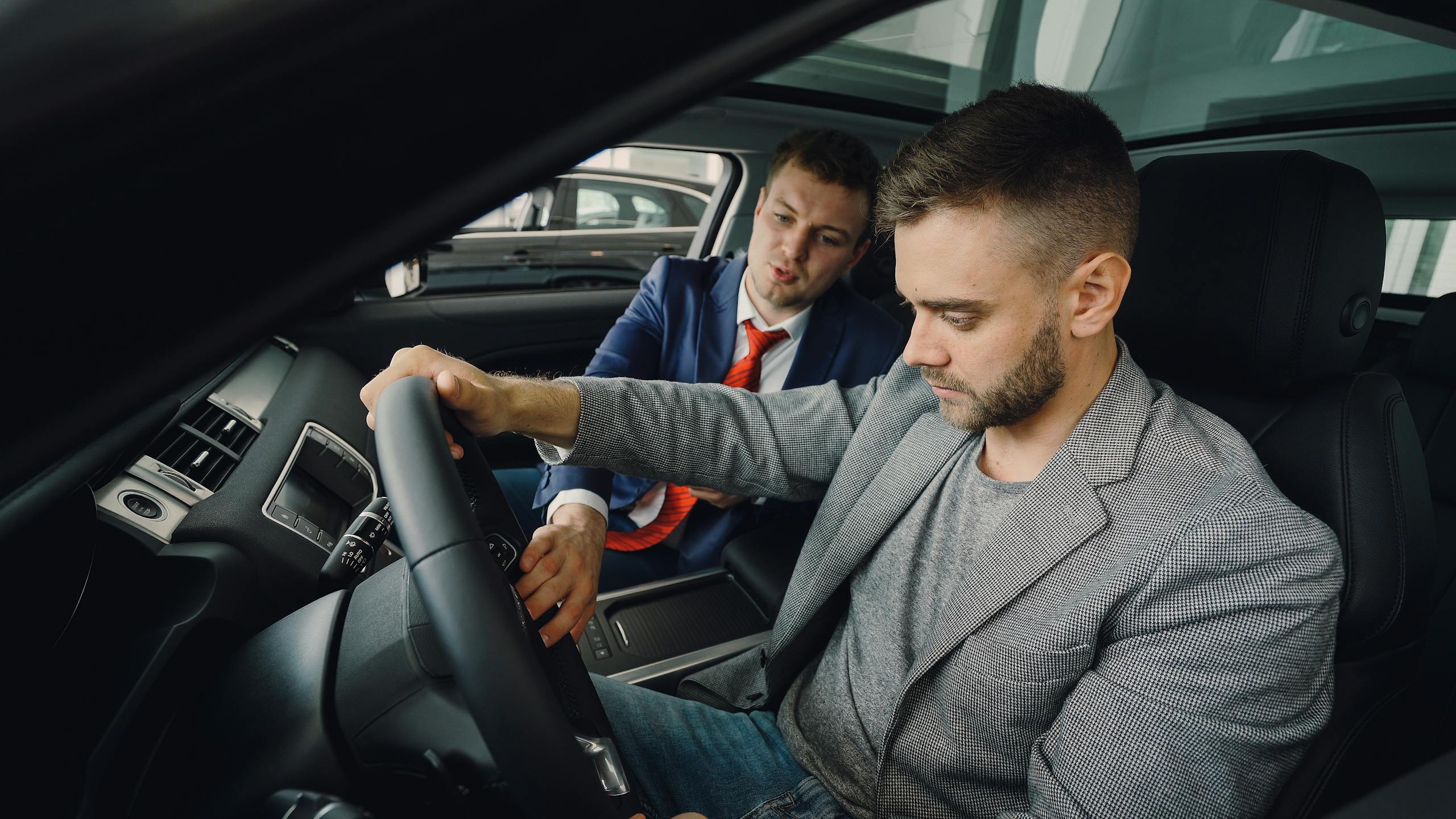 Salesman demonstrating car features to potential buyer inside vehicle showroom.