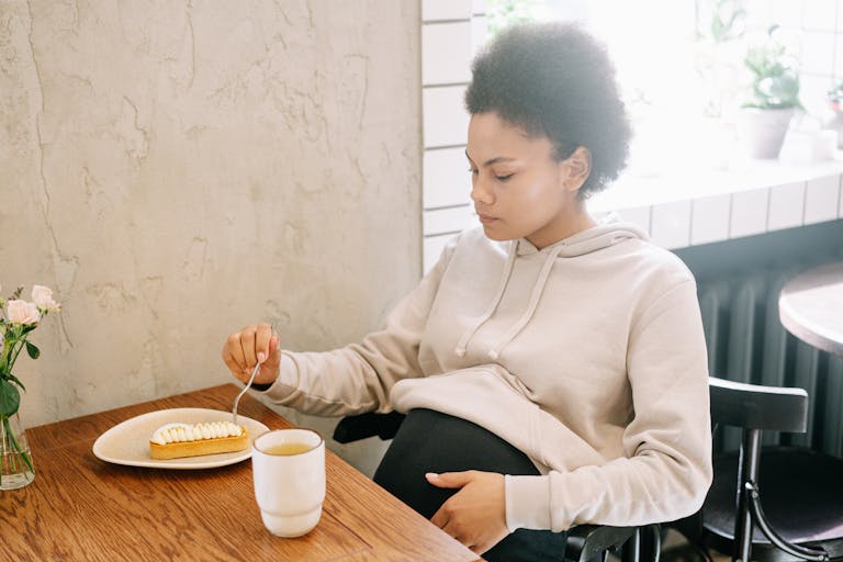 Serene pregnant woman in a cozy setting enjoying dessert and a hot drink.
