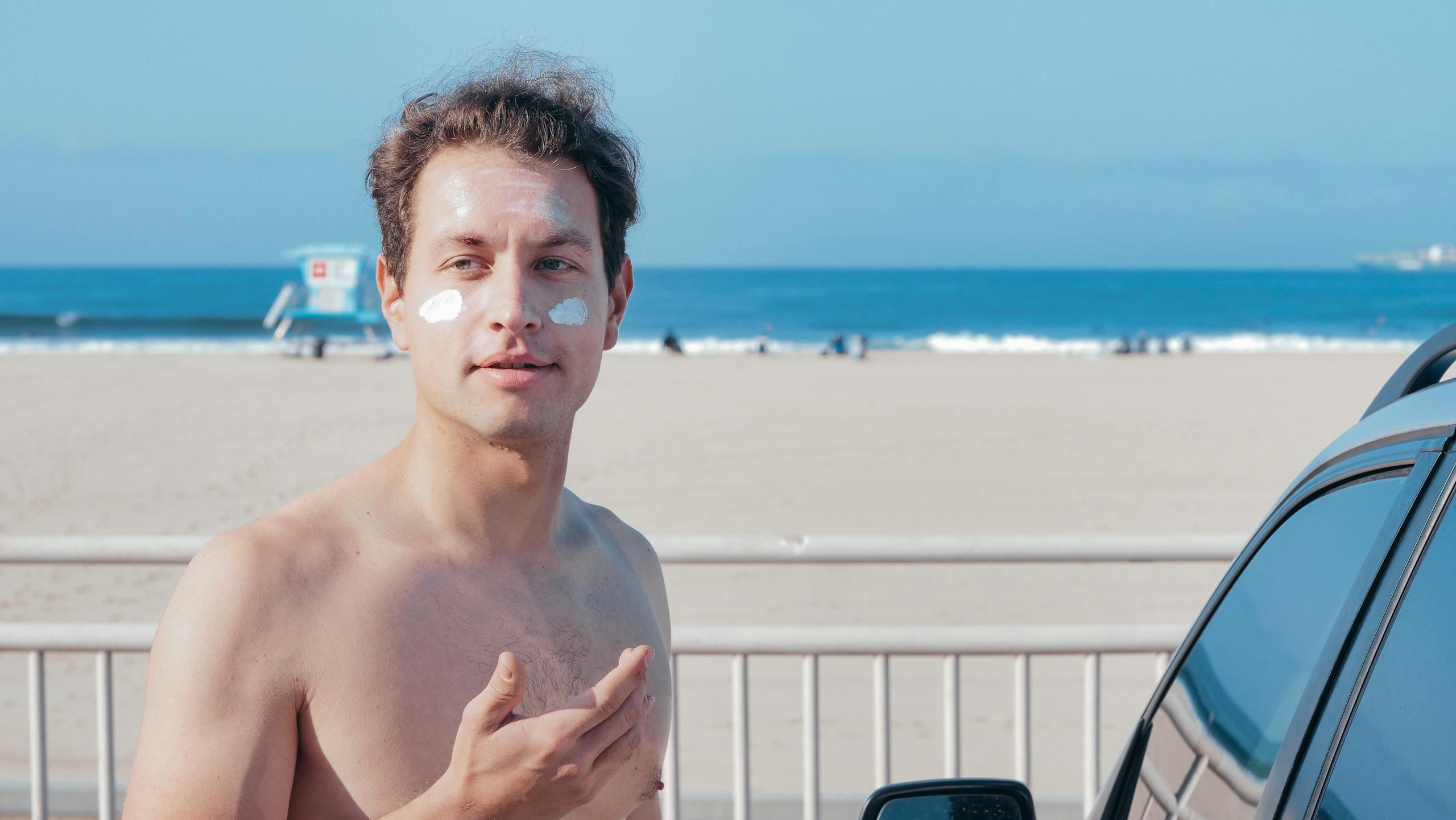 Shirtless man at the beach with sunscreen cream on his face, enjoying a sunny day.