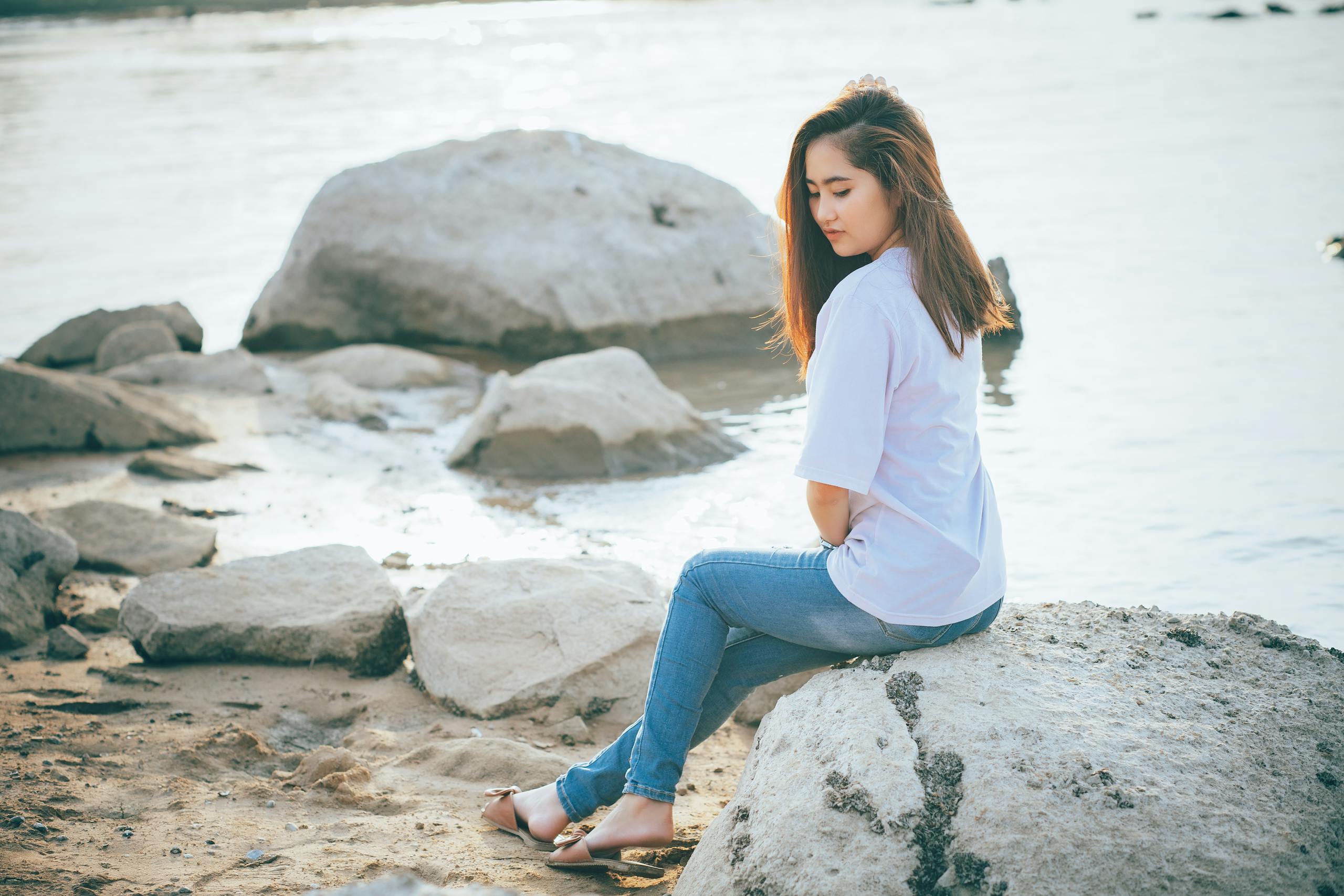 Side view of serene ethnic female resting on stone on shore of river and enjoying summer alone
