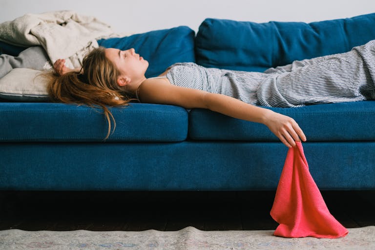 Side view of young exhausted woman with rag lying on couch in living room in daylight