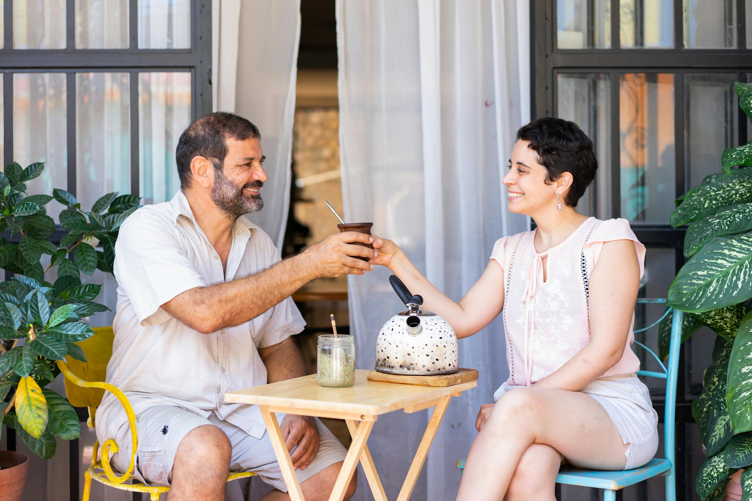 Smiling couple sharing a moment with yerba mate on a sunny patio.