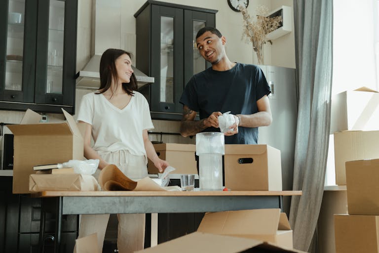 Smiling couple unpacking boxes in their new home kitchen, ready for a fresh start.