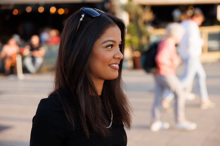 Smiling young woman with sunglasses outdoors on a sunny day.