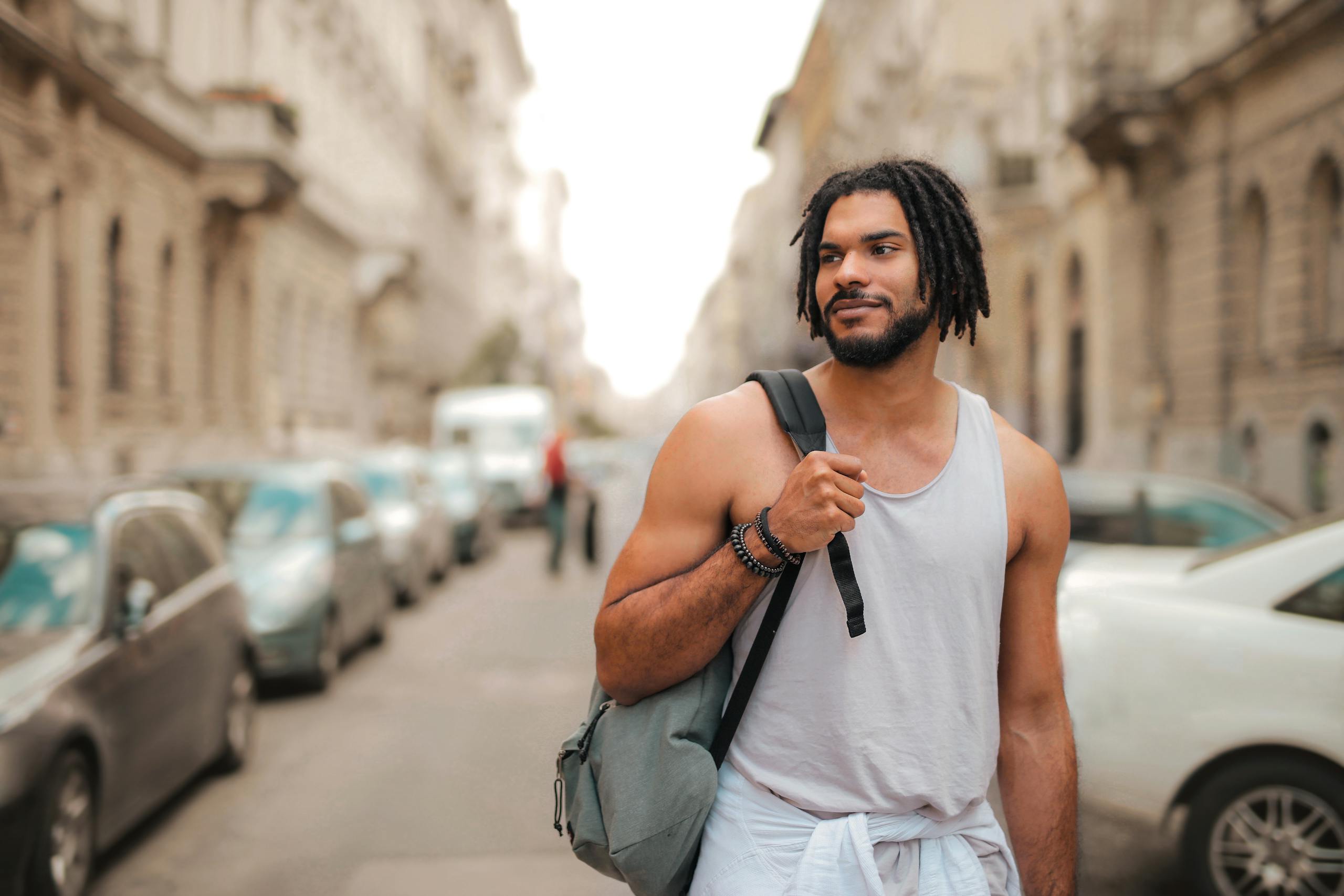 Stylish young man walking through an urban street, enjoying a sunny day outdoors.