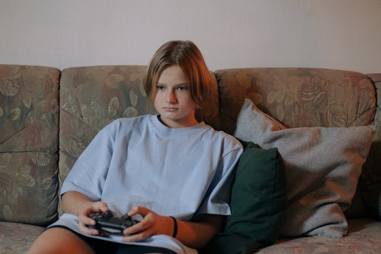 Teen girl sitting on a sofa playing video games with a controller, focused and relaxed.