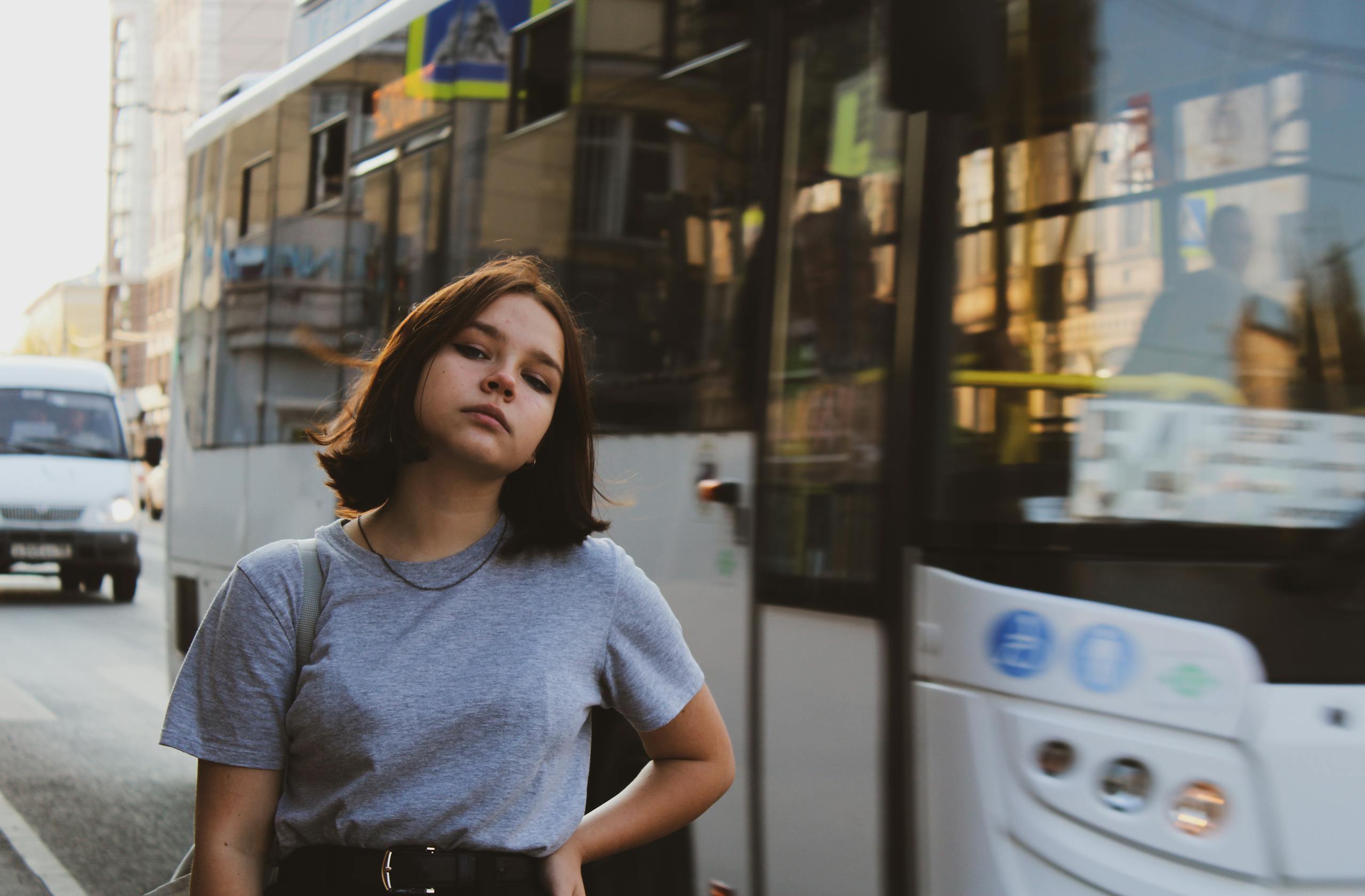 Teen girl standing confidently on city street near bus, capturing urban life essence.