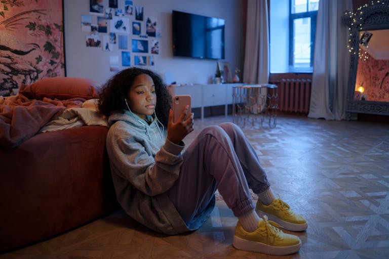Teenage girl sitting on the floor using a smartphone, relaxed in a cozy room setting.
