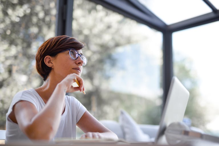 Thoughtful woman with glasses and short hair looking out window in a modern room.