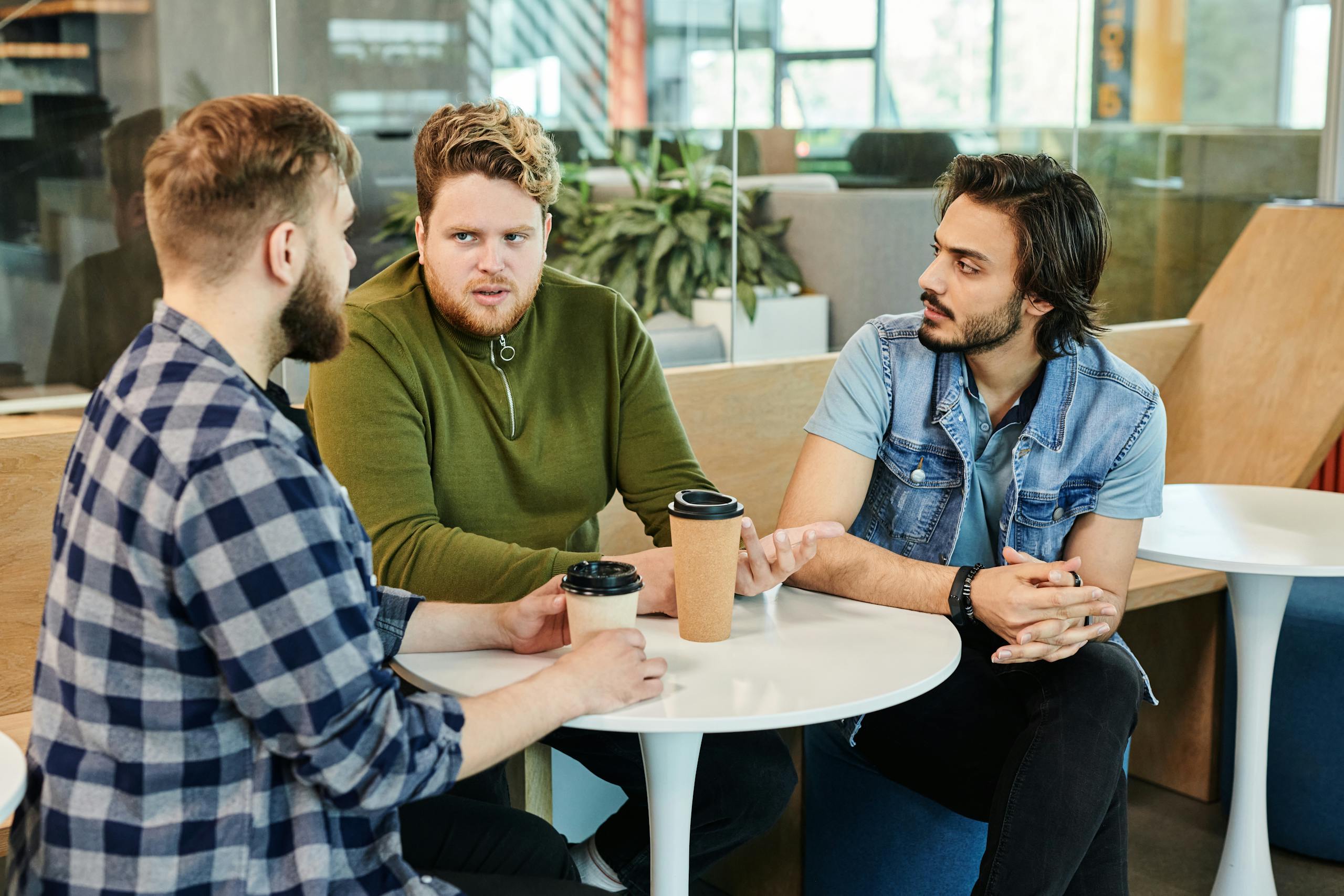 Three men having a casual business meeting in a cafe, engaging in conversation over coffee.