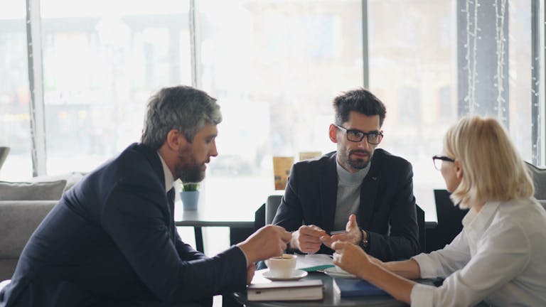 Three professionals engaging in a business discussion over coffee in a modern café setting.