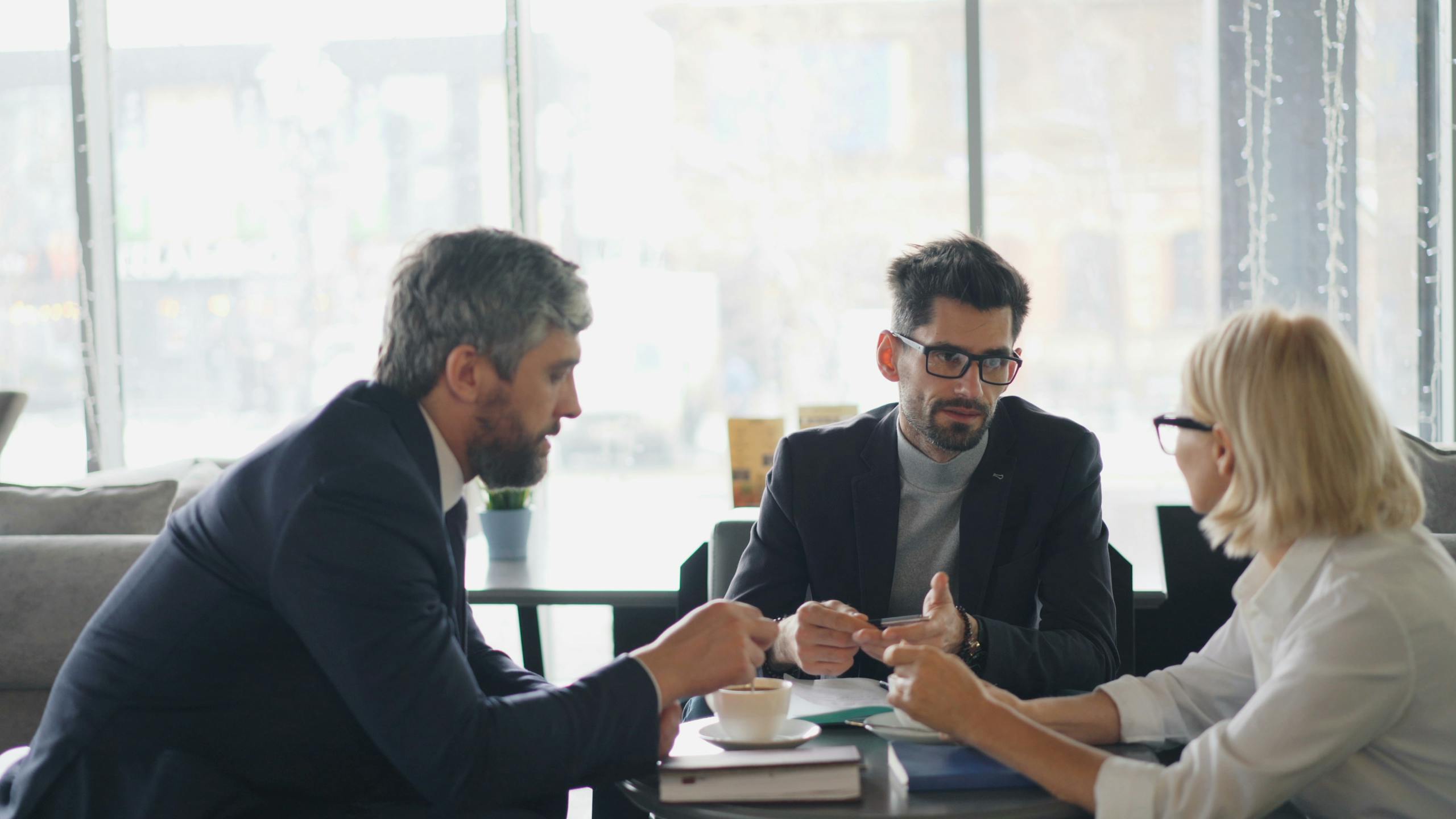Three professionals engaging in a business discussion over coffee in a modern café setting.