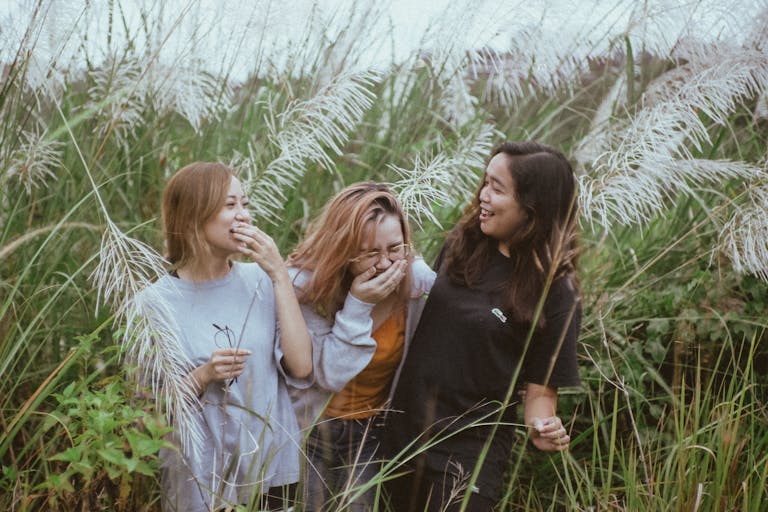 Three women enjoying a lighthearted moment amidst tall pampas grass in a natural outdoor setting.