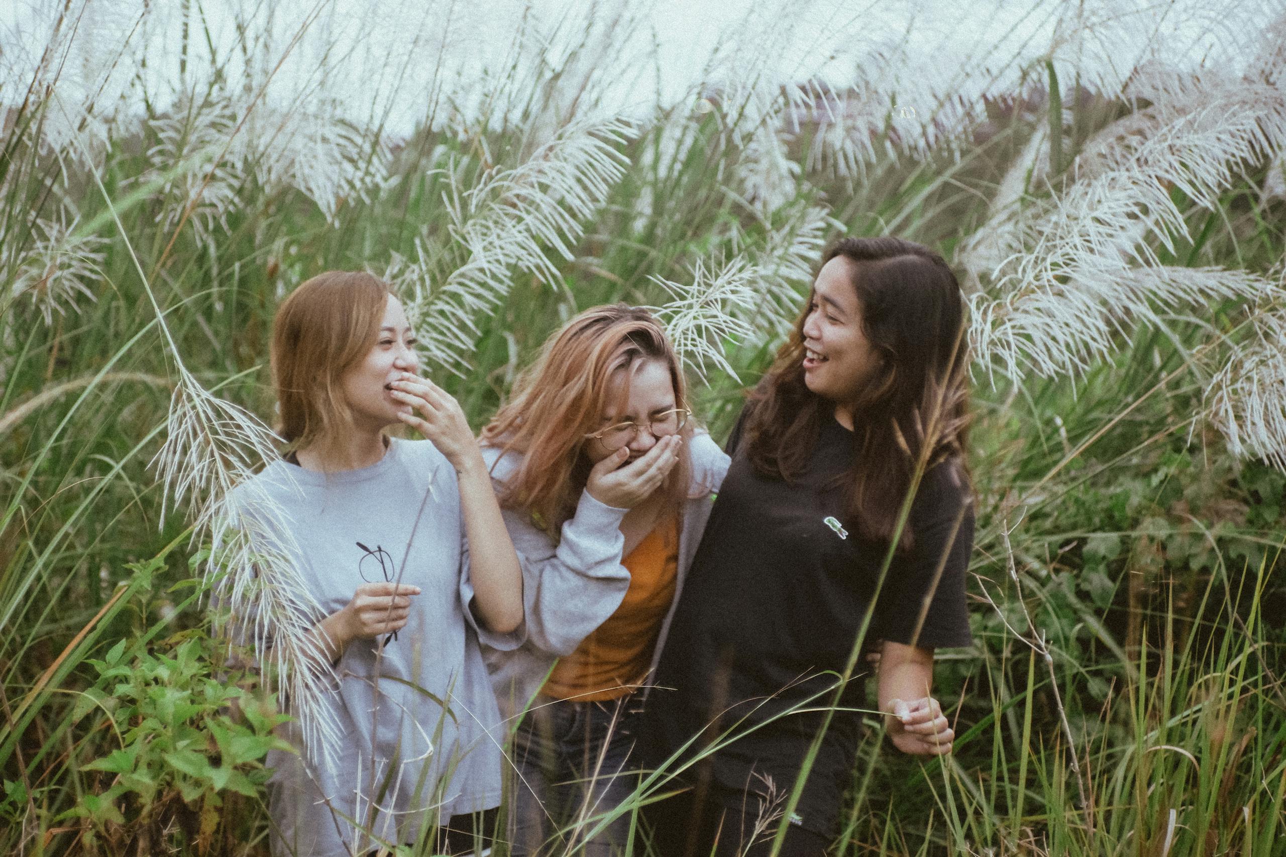 Three women enjoying a lighthearted moment amidst tall pampas grass in a natural outdoor setting.