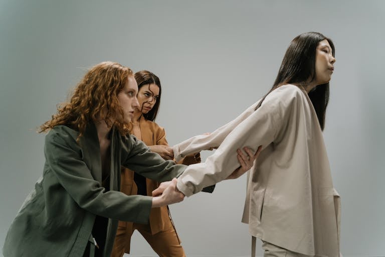 Three women in a conceptual studio shoot conveying struggle and connection.