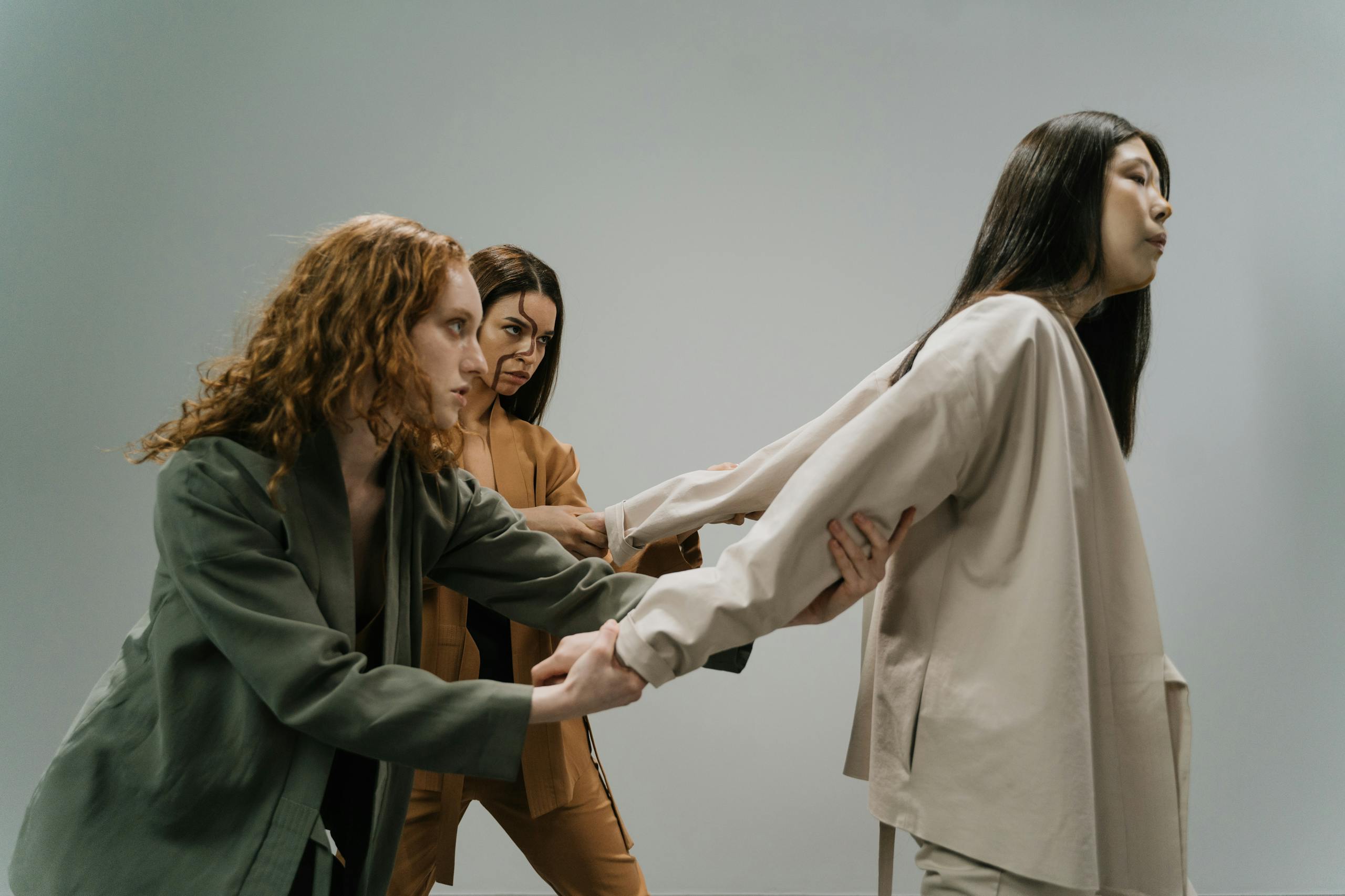 Three women in a conceptual studio shoot conveying struggle and connection.