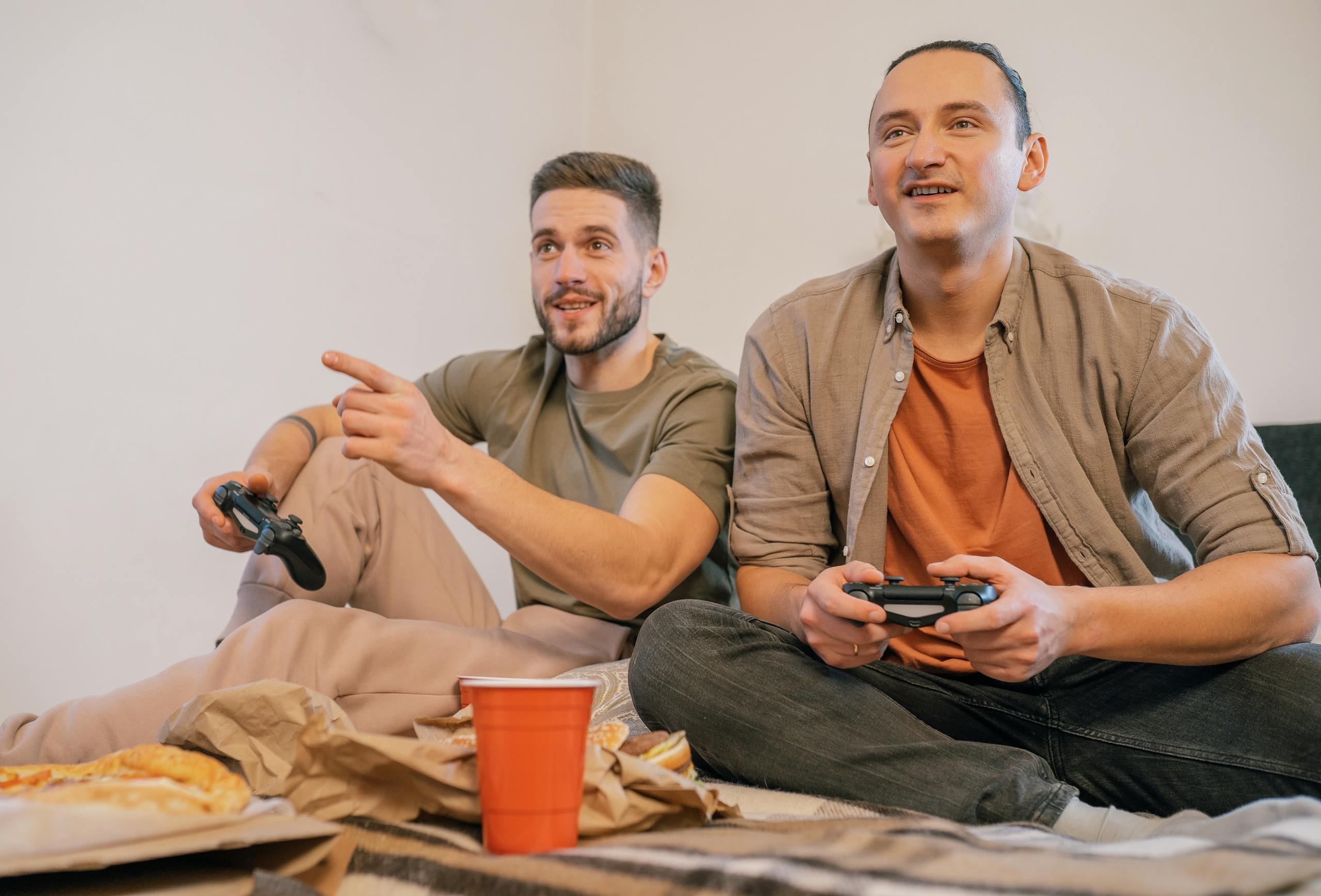 Two adult men sitting together playing video games with controllers, enjoying leisure time.