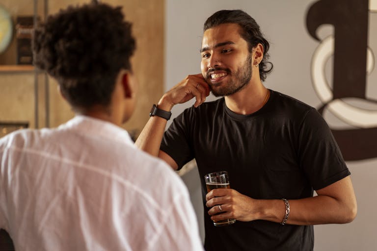 Two friends having a casual conversation indoors, one holding a drink.