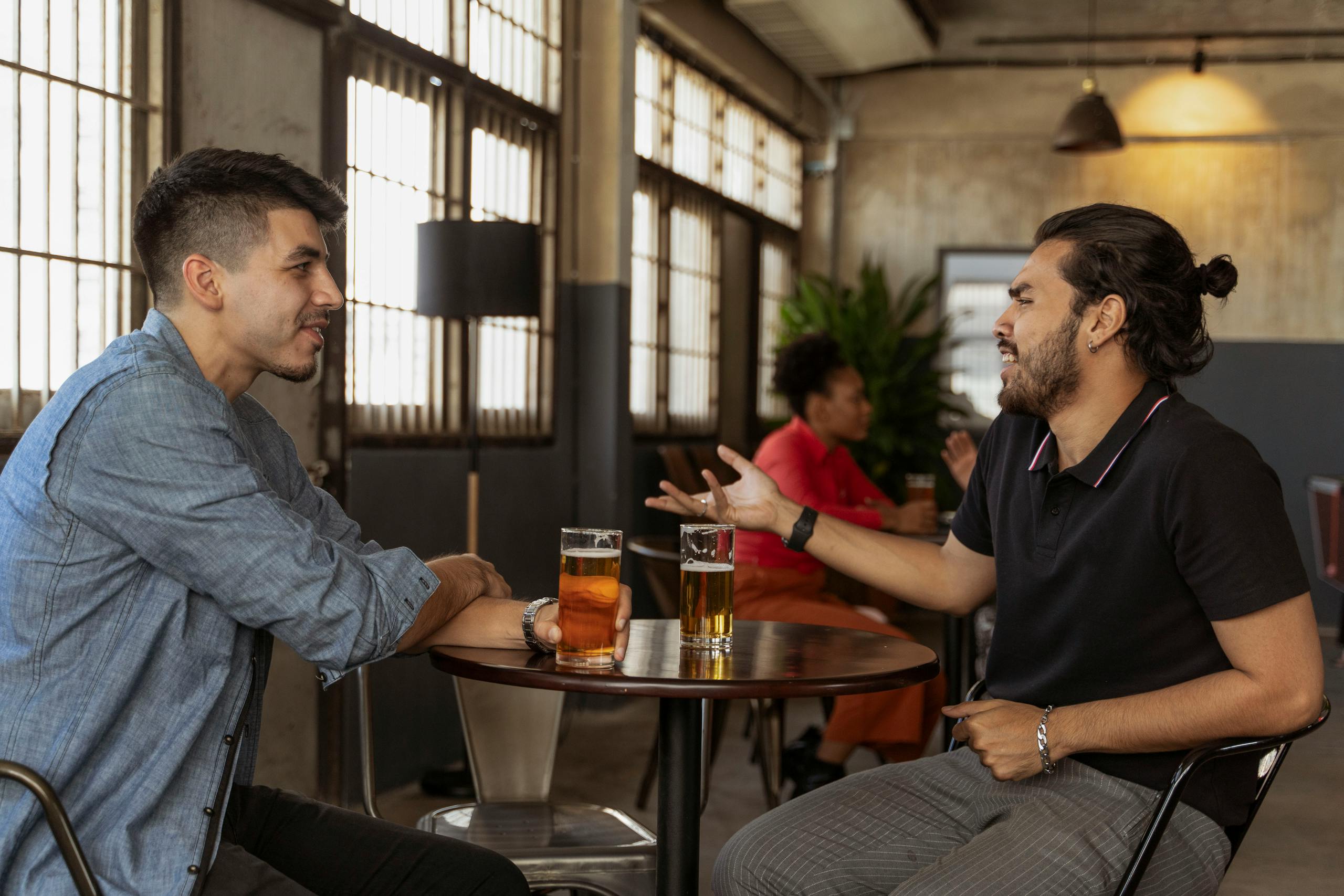 Two men engaging in a friendly conversation over beer at an indoor cafe setting.