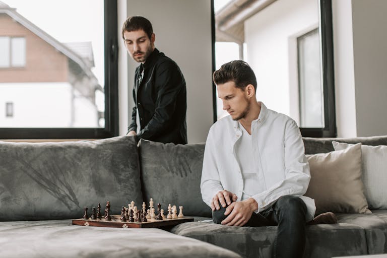 Two men playing chess on a couch, focusing on strategy inside a modern living room.