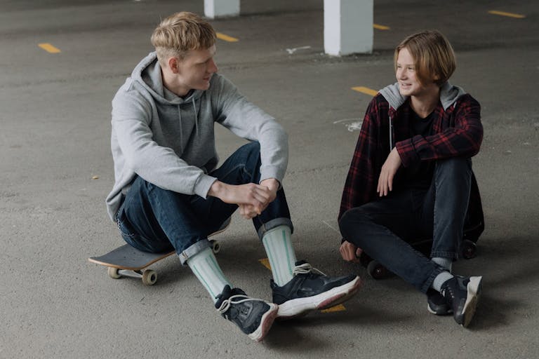 Two teenage skaters sitting and talking in a parking garage.