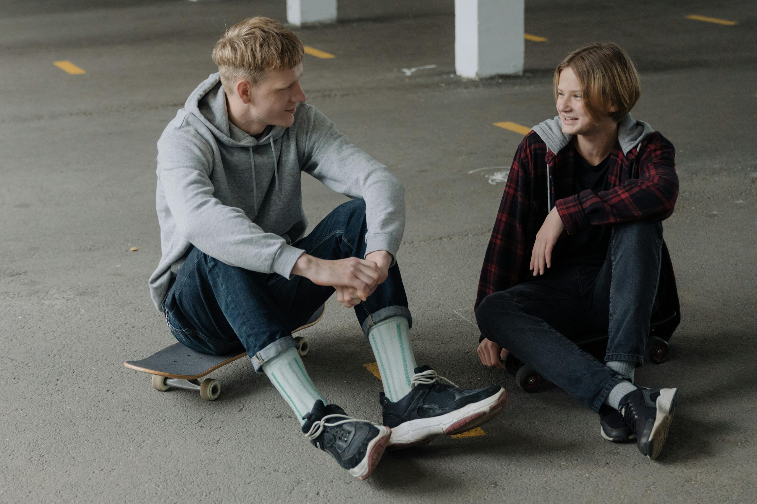Two teenage skaters sitting and talking in a parking garage.