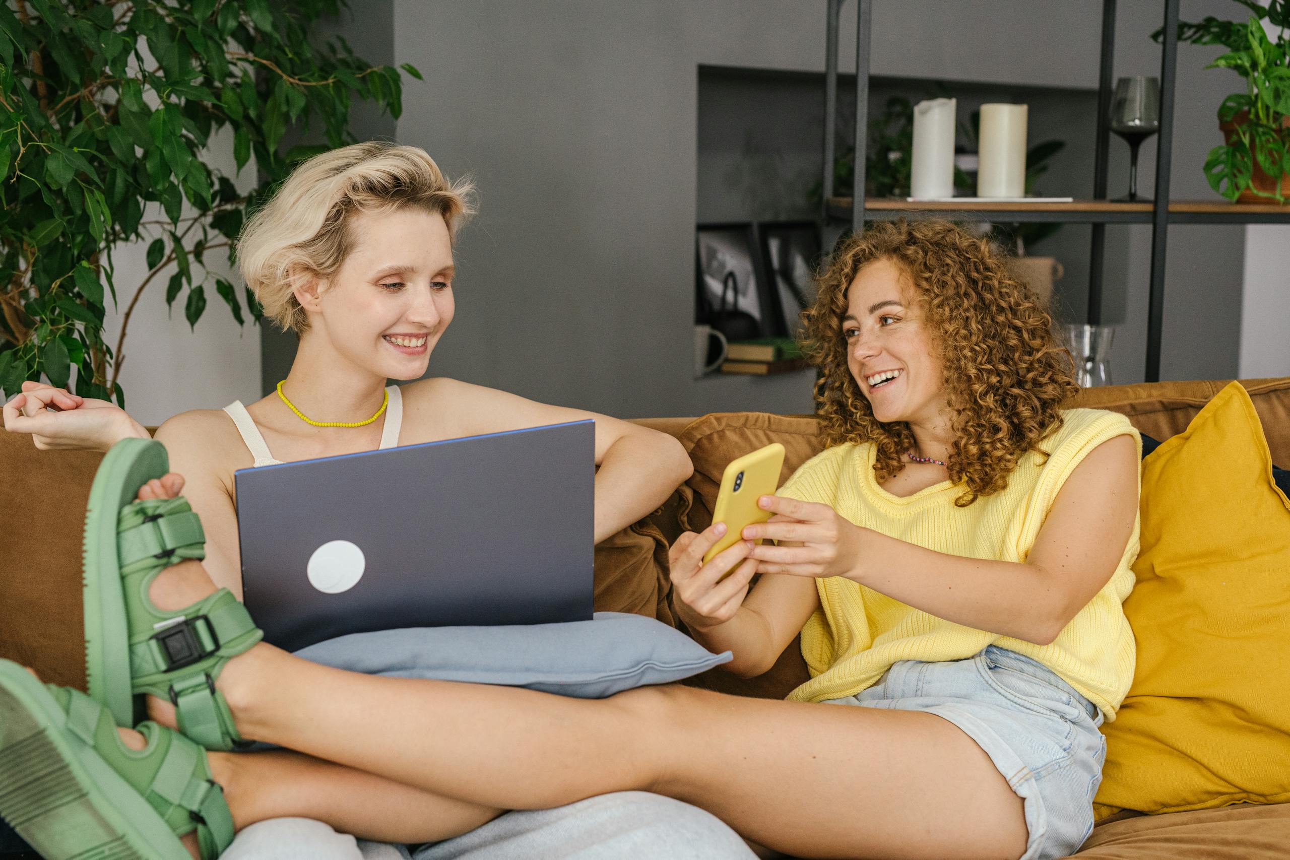 Two women happily sharing a moment on the couch, connected through technology.
