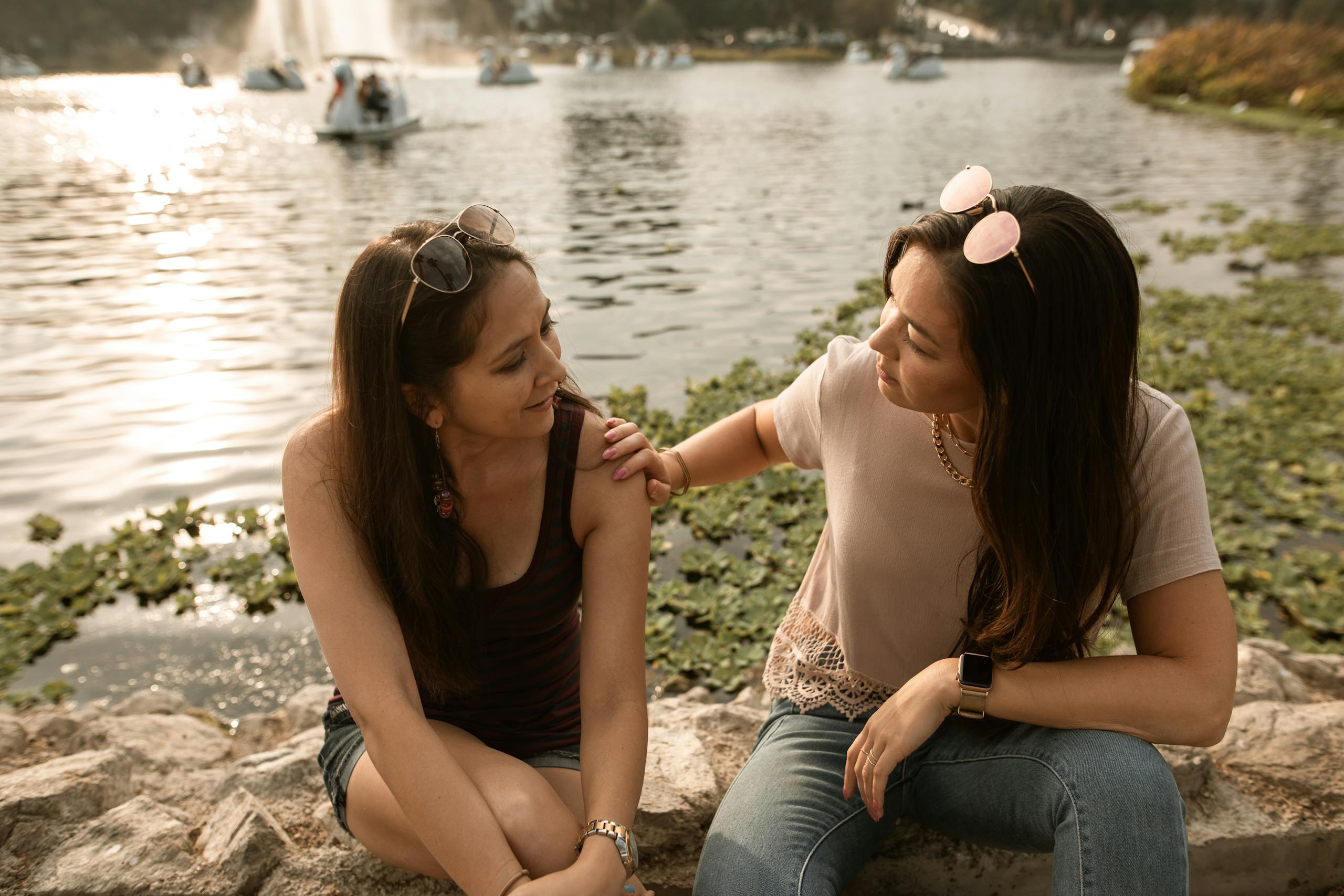 Two women having a heart-to-heart conversation by a sunny lakeside.