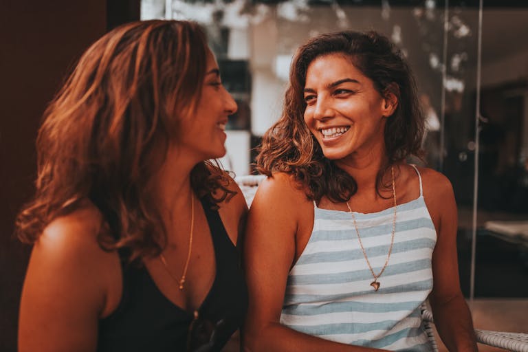 Two women smiling and enjoying a conversation indoors with a warm lighting ambiance.