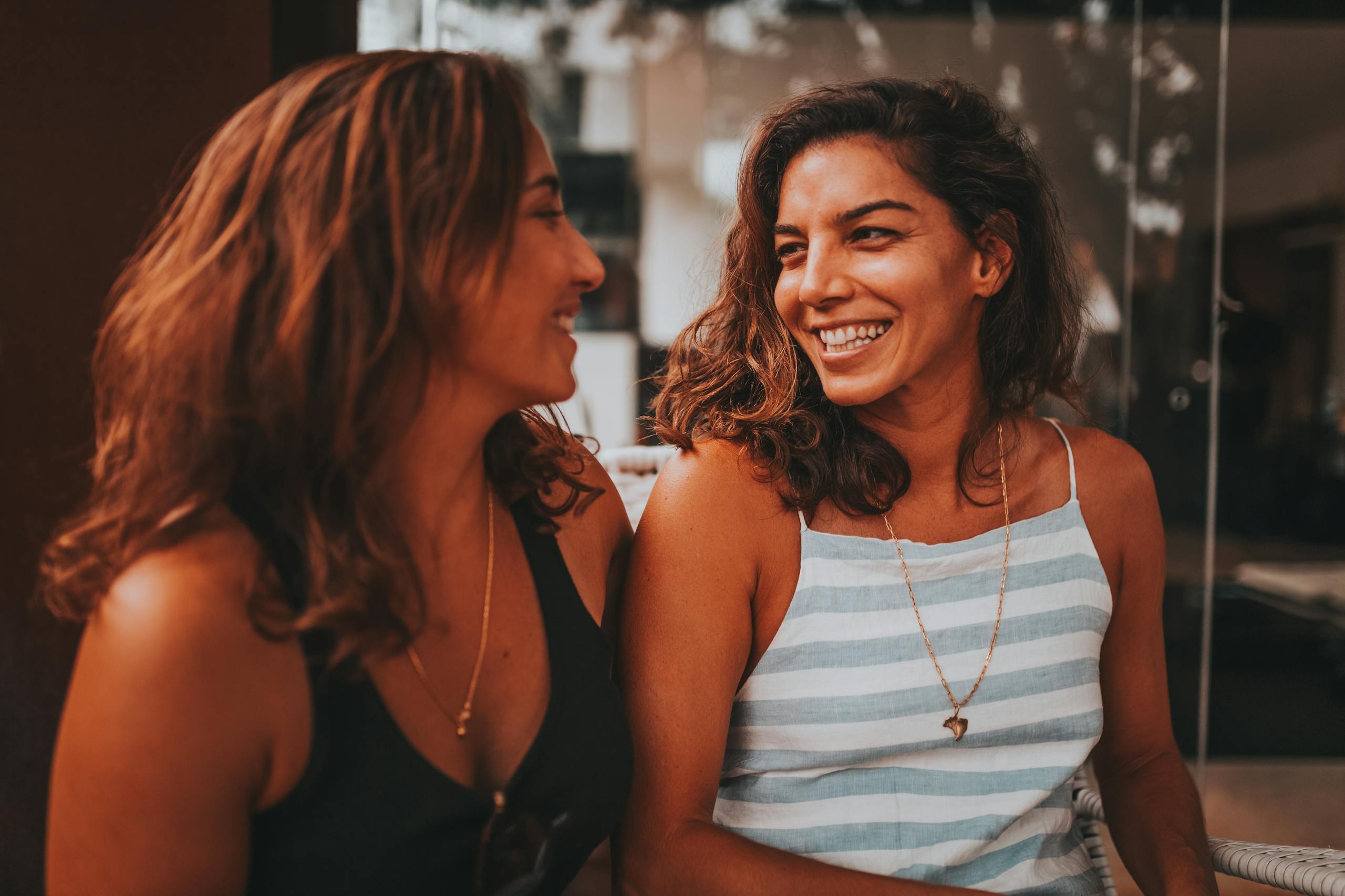 Two women smiling and enjoying a conversation indoors with a warm lighting ambiance.