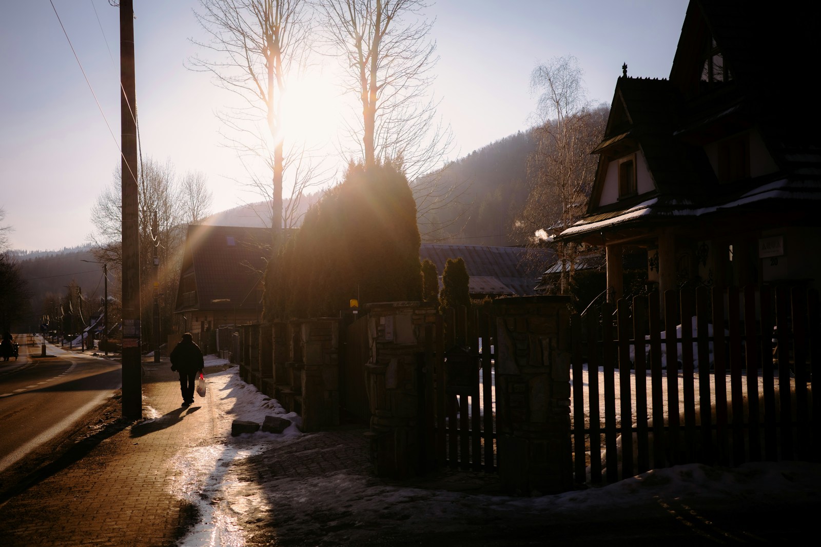 A person walks down a sunlit street in a village.