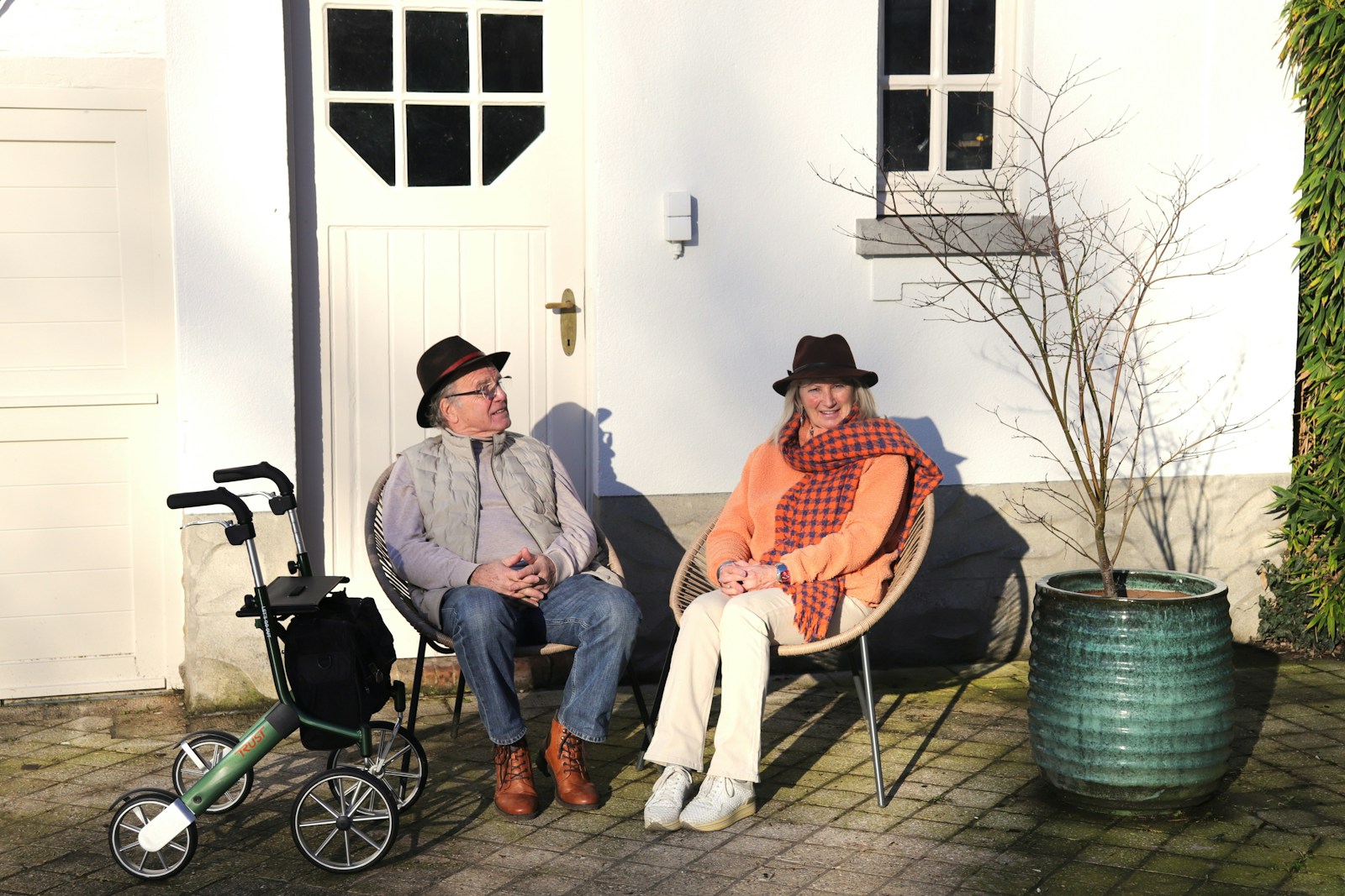 Elderly couple sitting outside with hats and walker