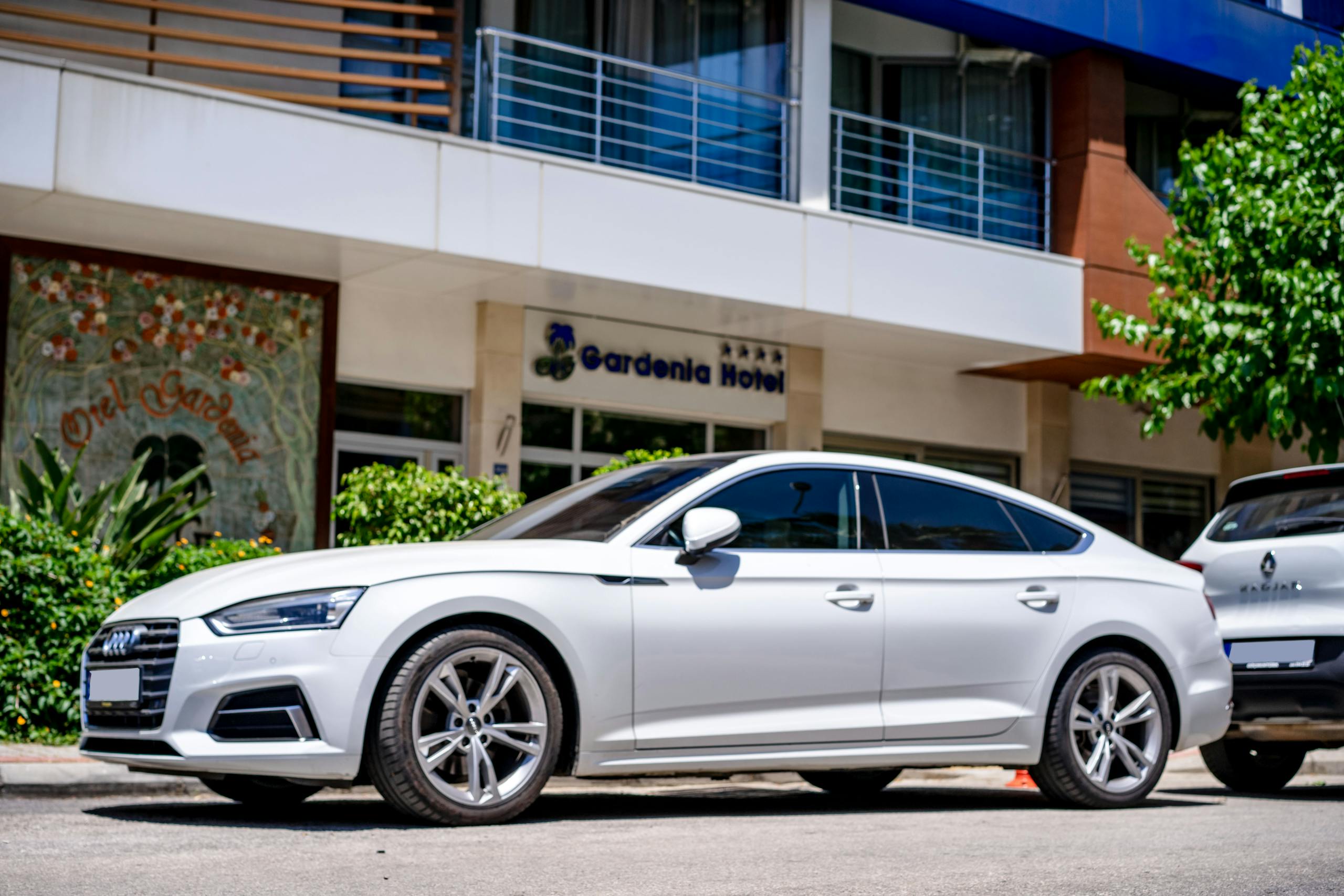 White luxury car parked in front of a hotel with modern architecture.