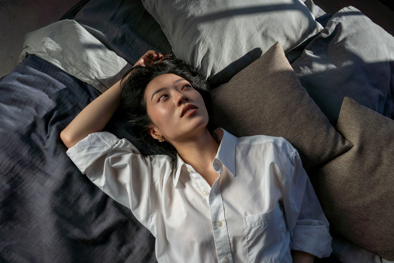 A woman in a white shirt lies on a bed.
