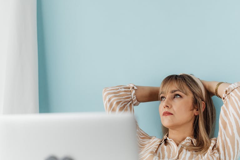 Woman in a striped blouse sitting with hands behind her head, contemplating while working remotely.